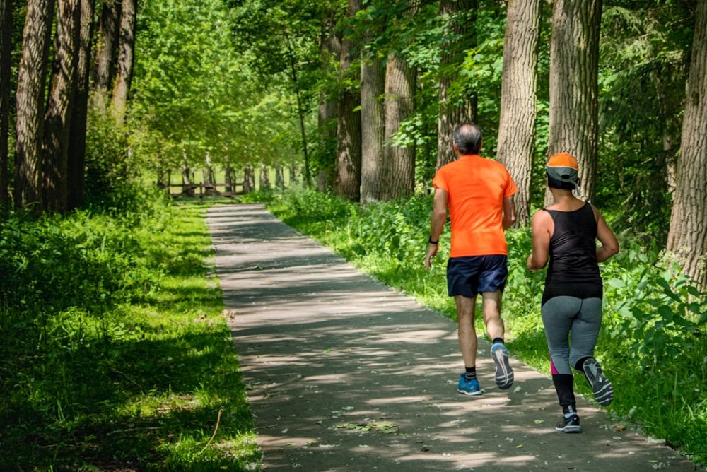 man in orange t-shirt and gray pants with blue shoes walking on pathway